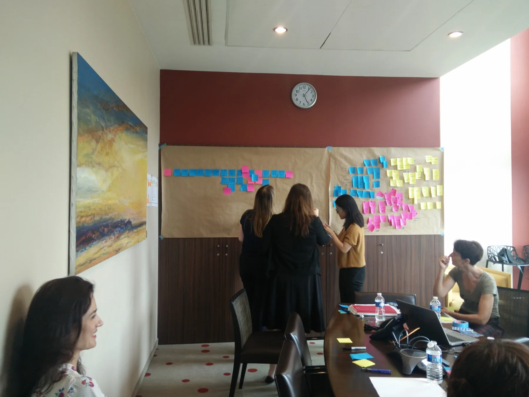 Participants building the research wall together, placing and grouping sticky notes on kraft paper